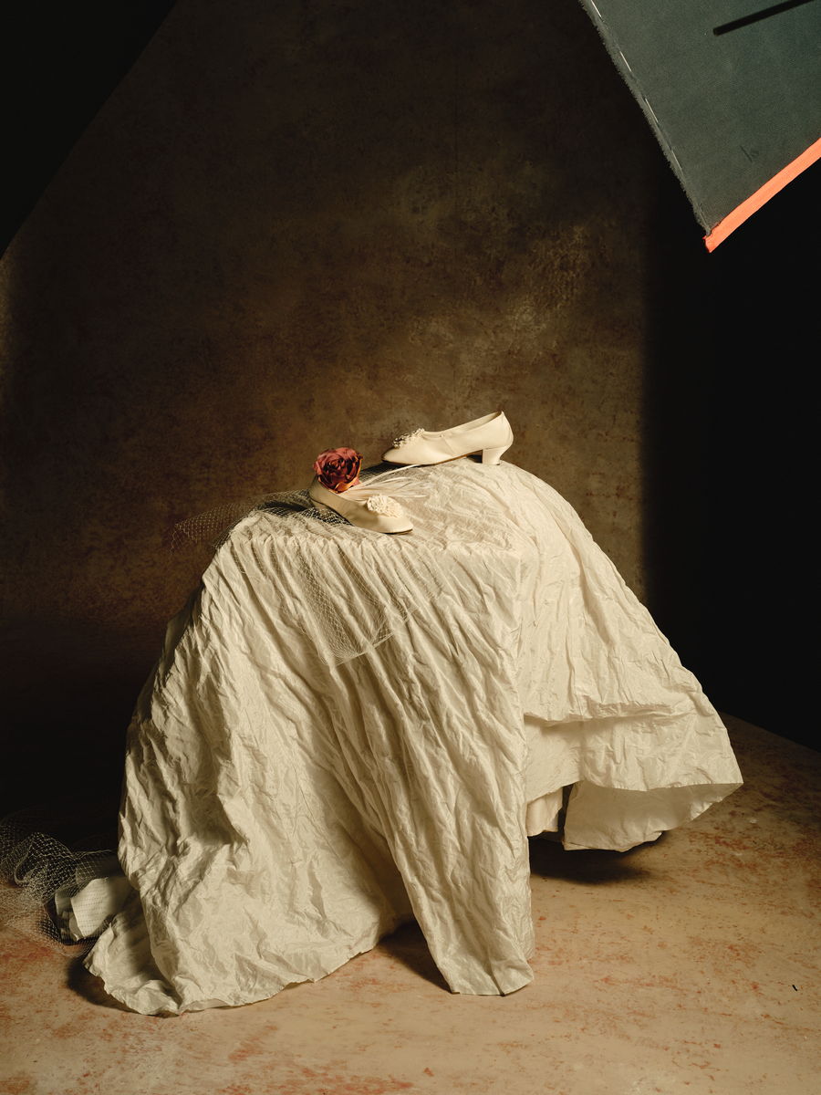 A silk wedding gown draped over a form, with satin shoes, a dried rose and veiling.